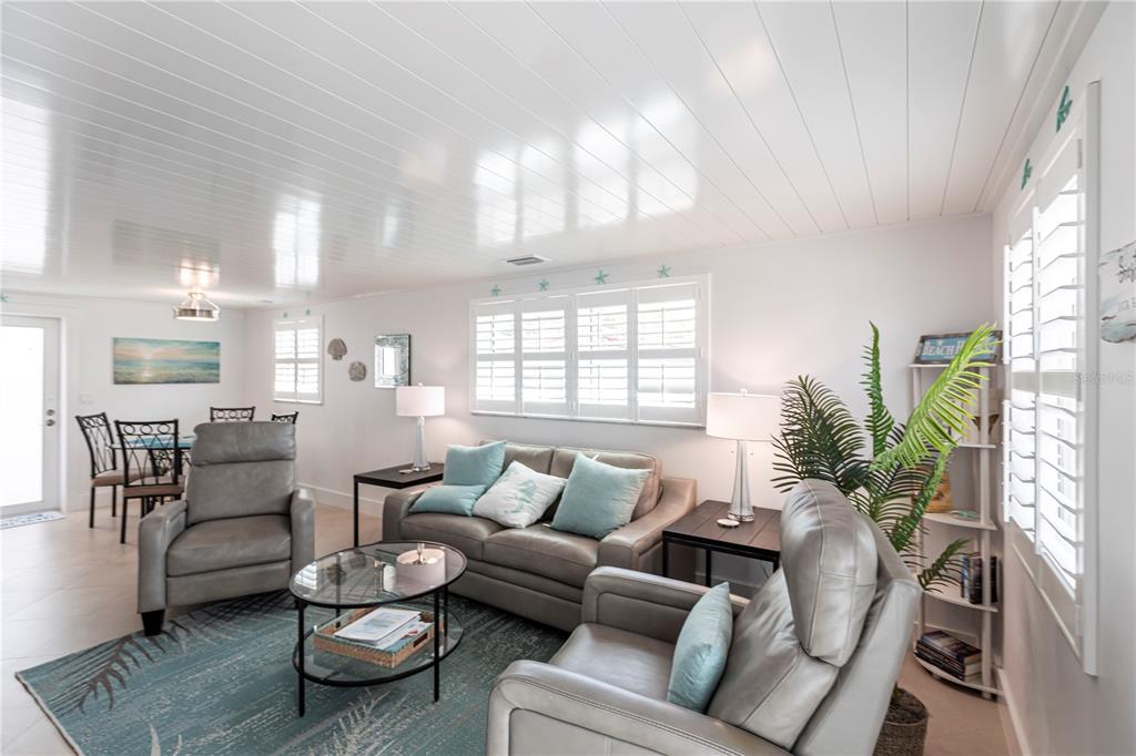 A living room features a gray sofa, two recliners, a glass coffee table, and white shutters — 6154 MIDNIGHT PASS ROAD UNIT A1, SARASOTA, FL