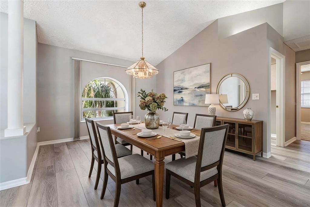 A dining room features a wooden table, gray upholstered chairs, a chandelier, and arched window — 1091 TOURNAMENT DRIVE, SPRING HILL, FL