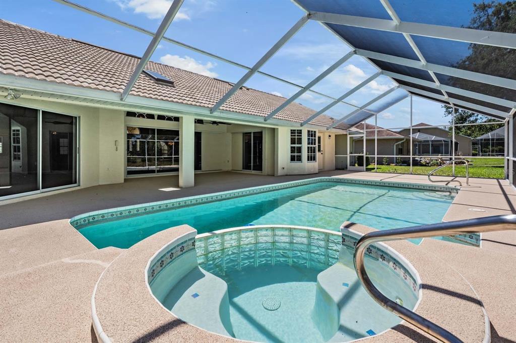 A screened-in patio features a swimming pool, a raised spa, and beige concrete decking — 1091 TOURNAMENT DRIVE, SPRING HILL, FL