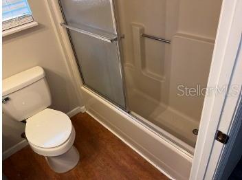A bathroom with a white toilet, a shower-tub combination, and wood-look flooring — 12450 SE 99TH AVENUE, BELLEVIEW, FL