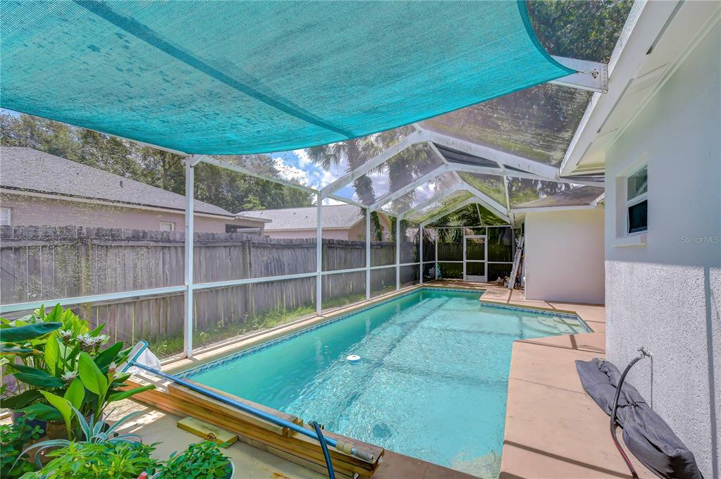 A swimming pool with a screen enclosure and a blue shade sail in a backyard — 4822 PORTOBELLO CIRCLE, VALRICO, FL