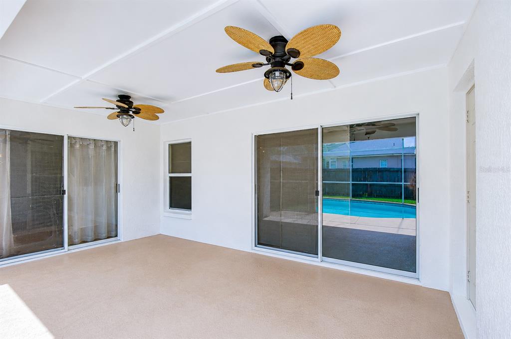 A covered patio features two ceiling fans, tan flooring, and sliding glass doors overlooking a pool — 4822 PORTOBELLO CIRCLE, VALRICO, FL