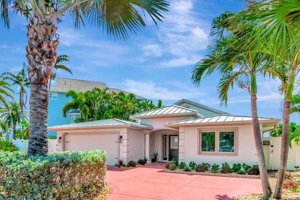 A single-story house with a metal roof, red driveway, and palm trees under a blue sky — 7025 BOCA CIEGA DRIVE, ST PETE BEACH, FL