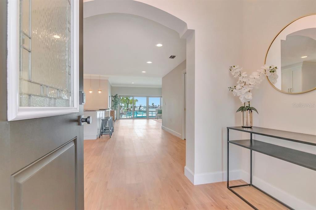 An entryway with light wood floors leads to an open-concept kitchen and waterfront living area — 7025 BOCA CIEGA DRIVE, ST PETE BEACH, FL