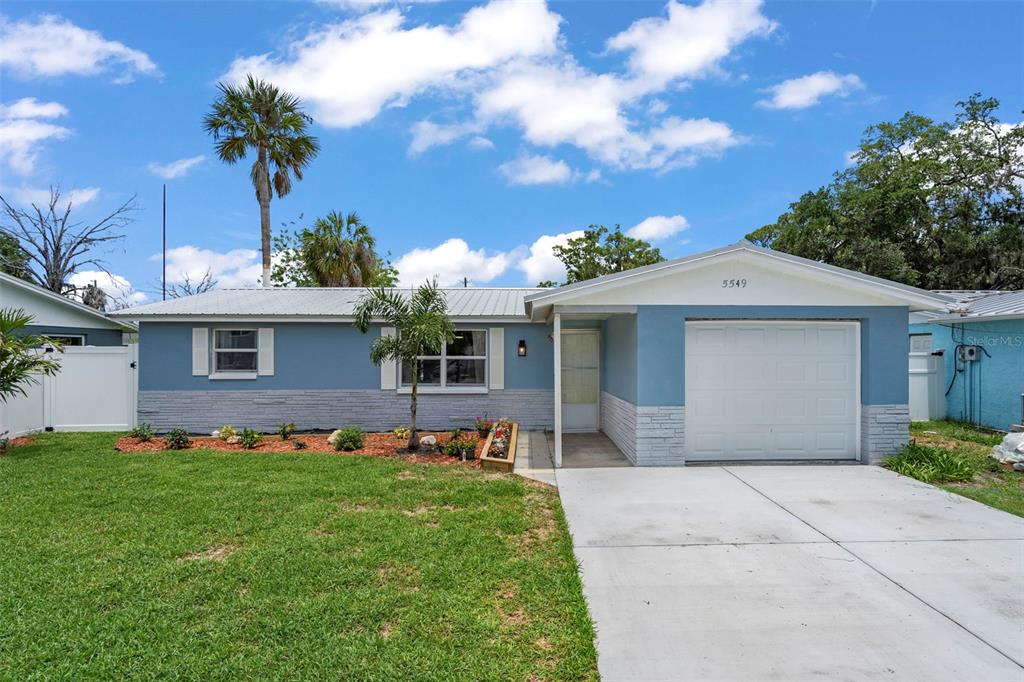 A single-story blue house with a white garage, metal roof, and a front lawn — 5549 QUIST DRIVE, PORT RICHEY, FL