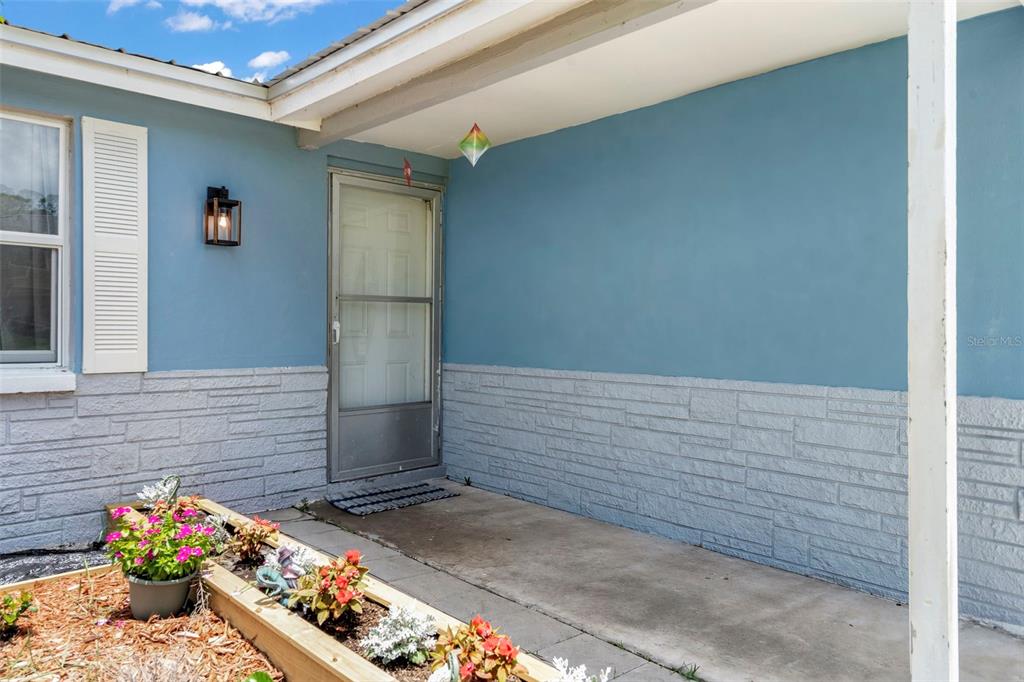 A blue house exterior features a concrete porch, a storm door, and a raised planter — 5549 QUIST DRIVE, PORT RICHEY, FL