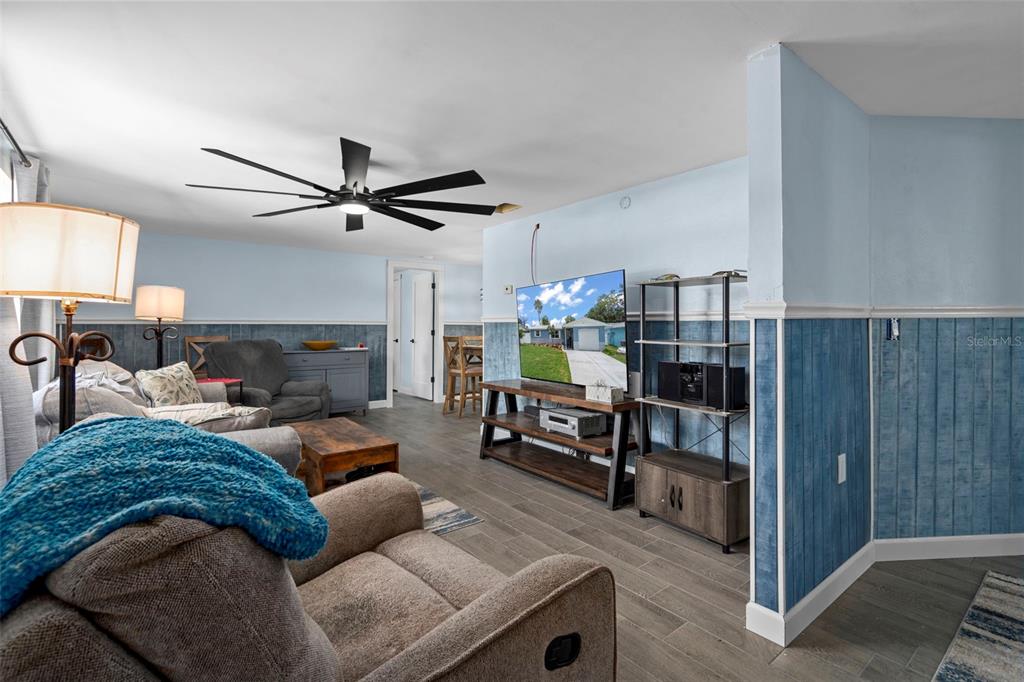 A living room features blue wainscoting, gray wood-look tile flooring, and a large ceiling fan — 5549 QUIST DRIVE, PORT RICHEY, FL