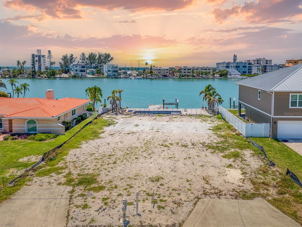 A vacant waterfront lot features a small pool and dock overlooking a bay at sunset — 10126 TARPON DRIVE, TREASURE ISLAND, FL