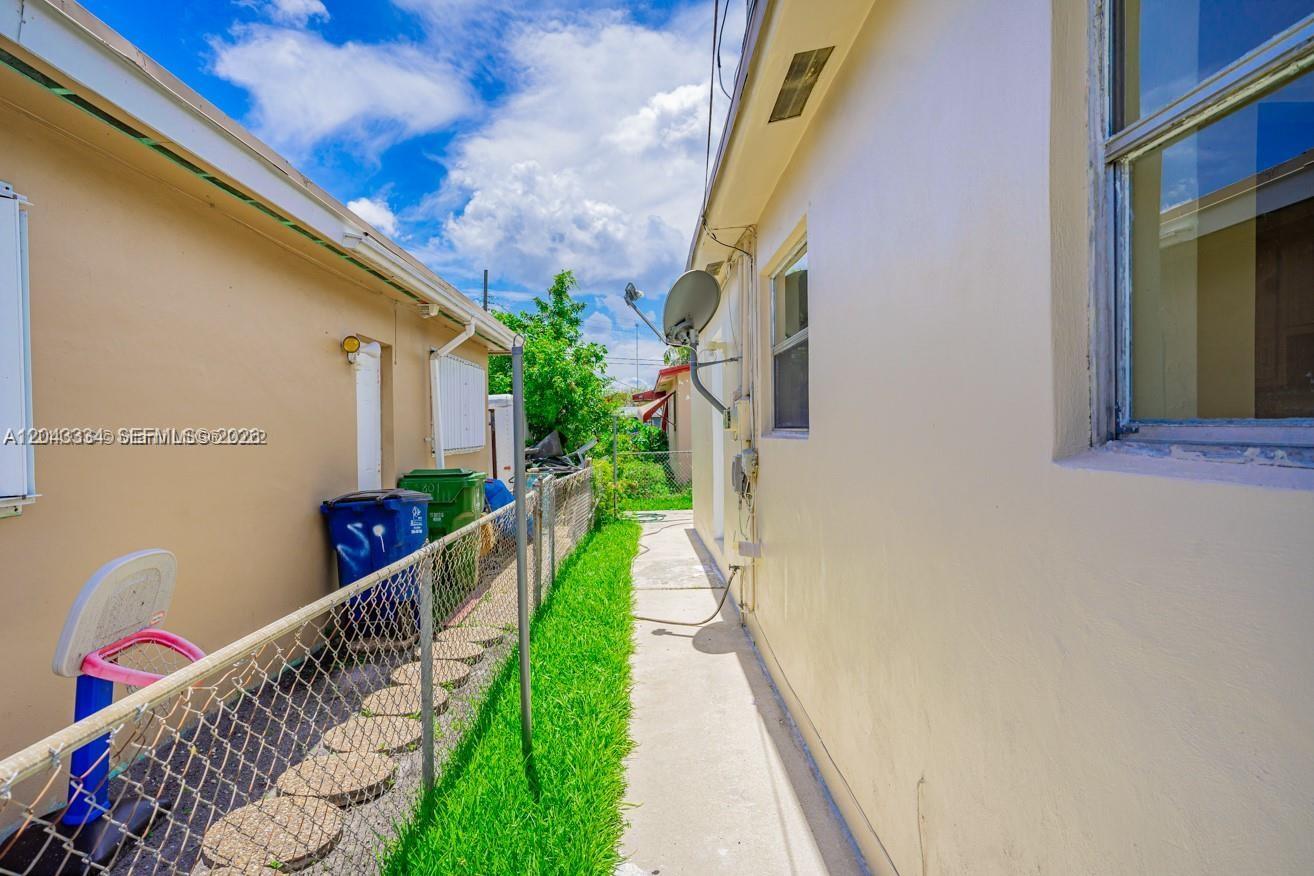 A narrow concrete walkway runs between two beige exterior walls separated by a chain-link fence — 805 NW 3rd Ter, Hallandale Beach FL 33009, HALLANDALE BEACH, FL