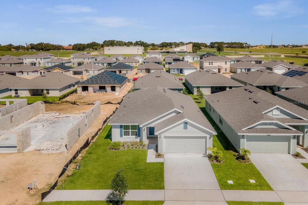 An aerial view shows a suburban neighborhood with single-family homes and a construction site — 671 TANARO LANE, HAINES CITY, FL