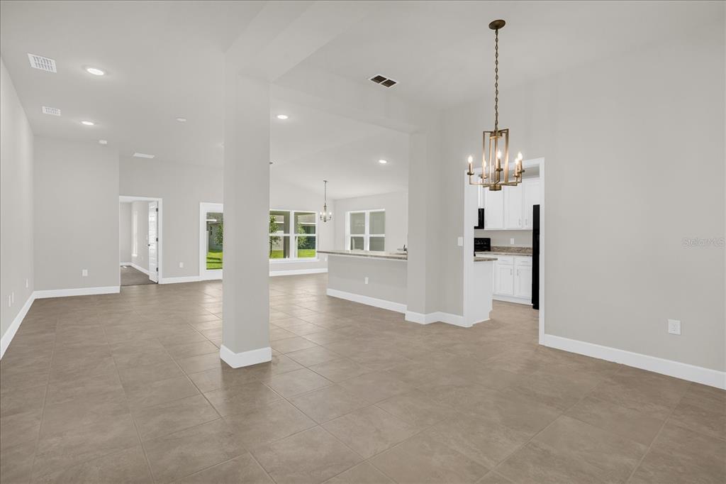 An open-concept living and dining area features neutral tile flooring and a modern chandelier — 671 TANARO LANE, HAINES CITY, FL