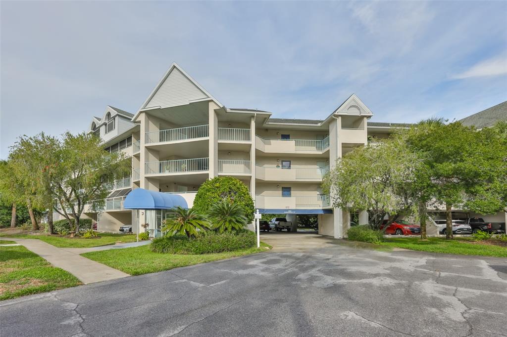 A multi-story apartment building features balconies, a blue awning, and a paved parking area — 5567 SEA FOREST DRIVE UNIT 122, NEW PORT RICHEY, FL
