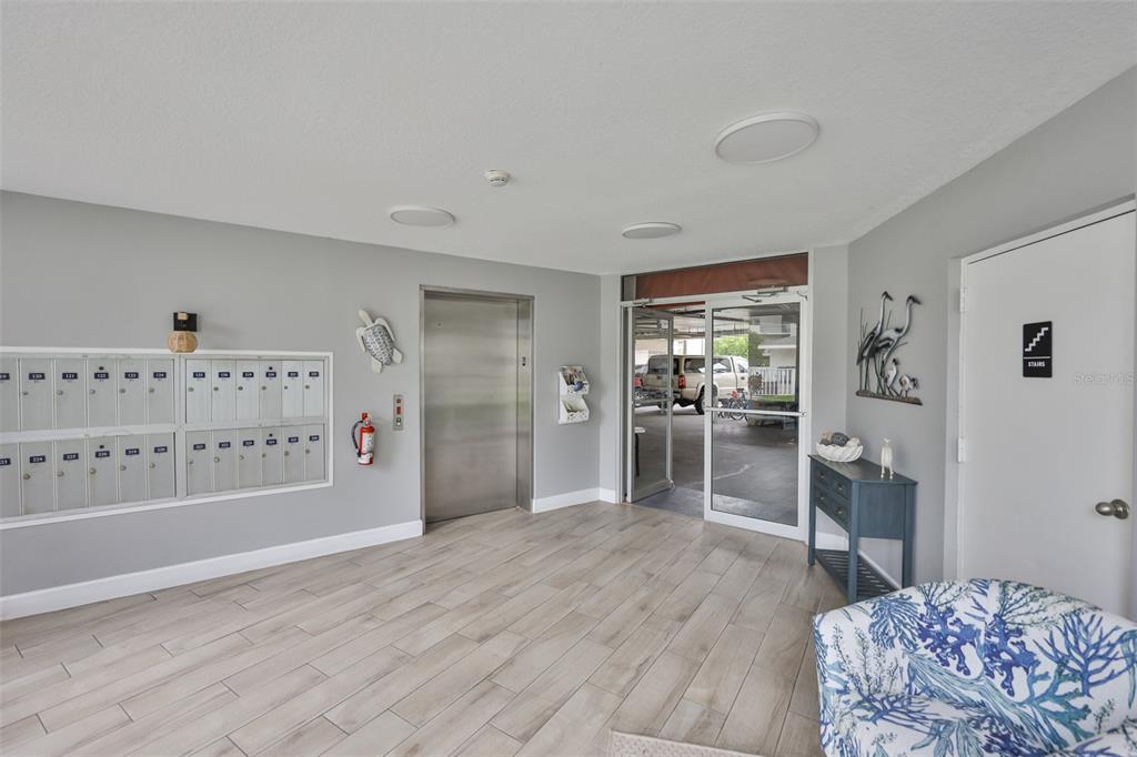 An apartment building lobby features gray walls, tile flooring, mailboxes, an elevator, and glass doors — 5567 SEA FOREST DRIVE UNIT 122, NEW PORT RICHEY, FL