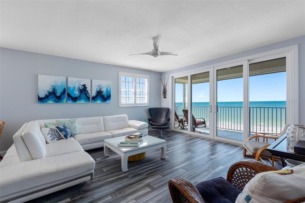 A living room features a white sectional sofa, wood-look flooring, and sliding doors overlooking the ocean — 19710 GULF BOULEVARD UNIT 301, INDIAN SHORES, FL