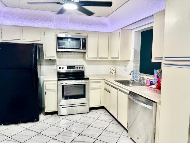 A kitchen with off-white cabinets, stainless steel appliances, a black refrigerator, and tiled floors — 18730 Stewart Circle # 5, Boca Raton FL 33496, BOCA RATON, FL