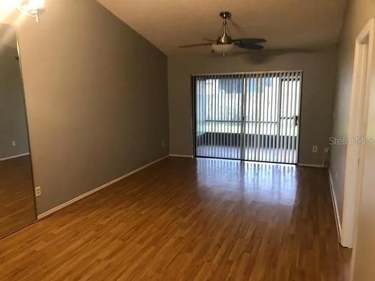 A living room features wood-look flooring, a vaulted ceiling with a fan, and sliding glass doors — 64 SILVER PARK CIRCLE, KISSIMMEE, FL
