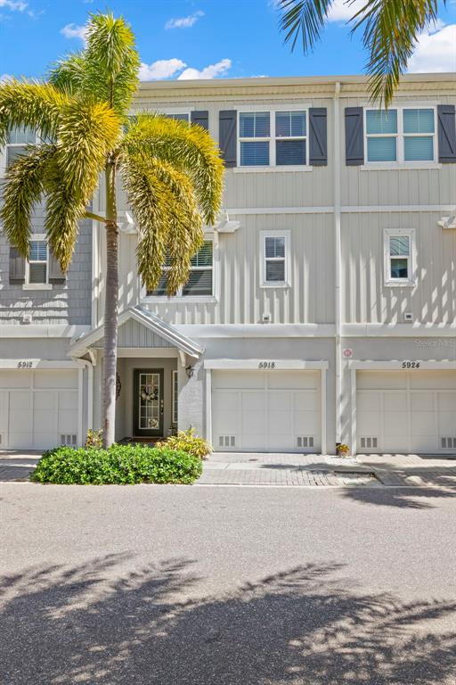 A multi-story townhouse exterior features light gray vertical siding, white garage doors, and a palm tree — 5918 ANCHORAGE WAY S, ST PETERSBURG, FL