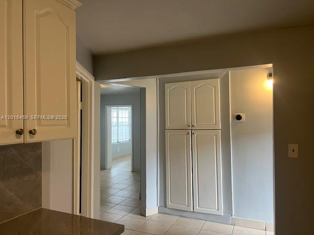 A kitchen with white cabinets opens into a hallway with tiled floors and built-in storage — 732 Moffett # 4A, Hallandale Beach FL 33009, HALLANDALE BEACH, FL