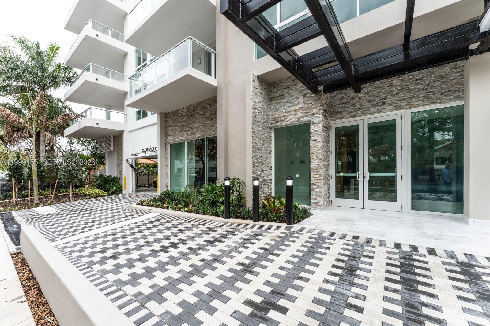 The exterior of a modern building features a paved driveway, stone accents, and glass doors — 1850 Monroe St # 410, Hollywood FL 33020, HOLLYWOOD, FL