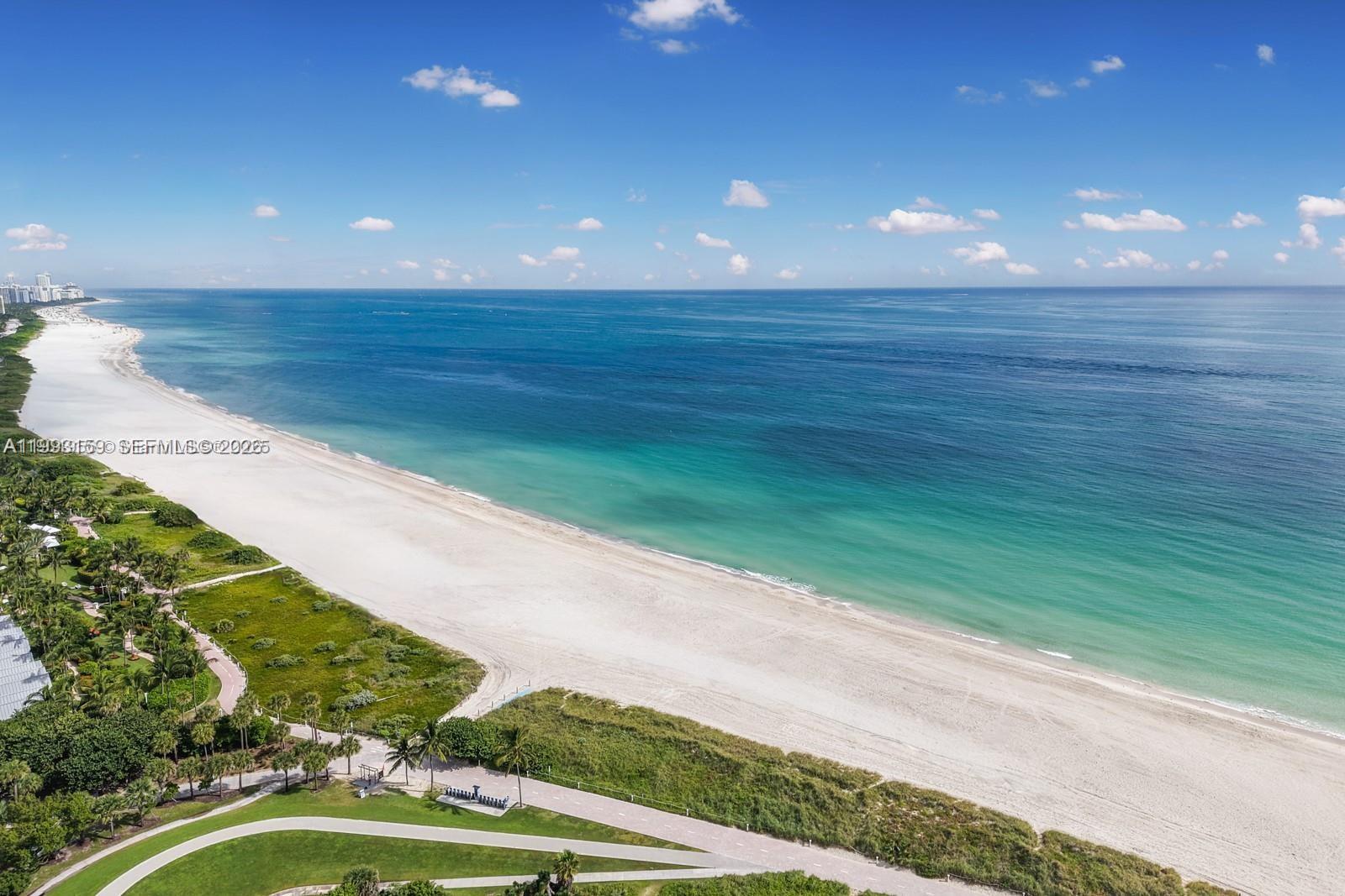 An aerial view shows a white sand beach meeting the turquoise ocean along a coastline — 300 S Pointe Drive # 801, Miami Beach FL 33139, MIAMI BEACH, FL