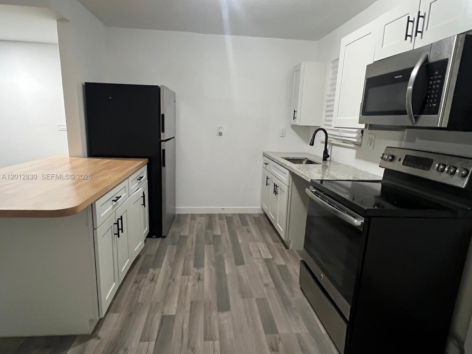 A kitchen features white cabinets, black appliances, a wood-topped island, and grey wood-look flooring — 1560 NE 151st St # 102, Miami FL 33162, MIAMI, FL