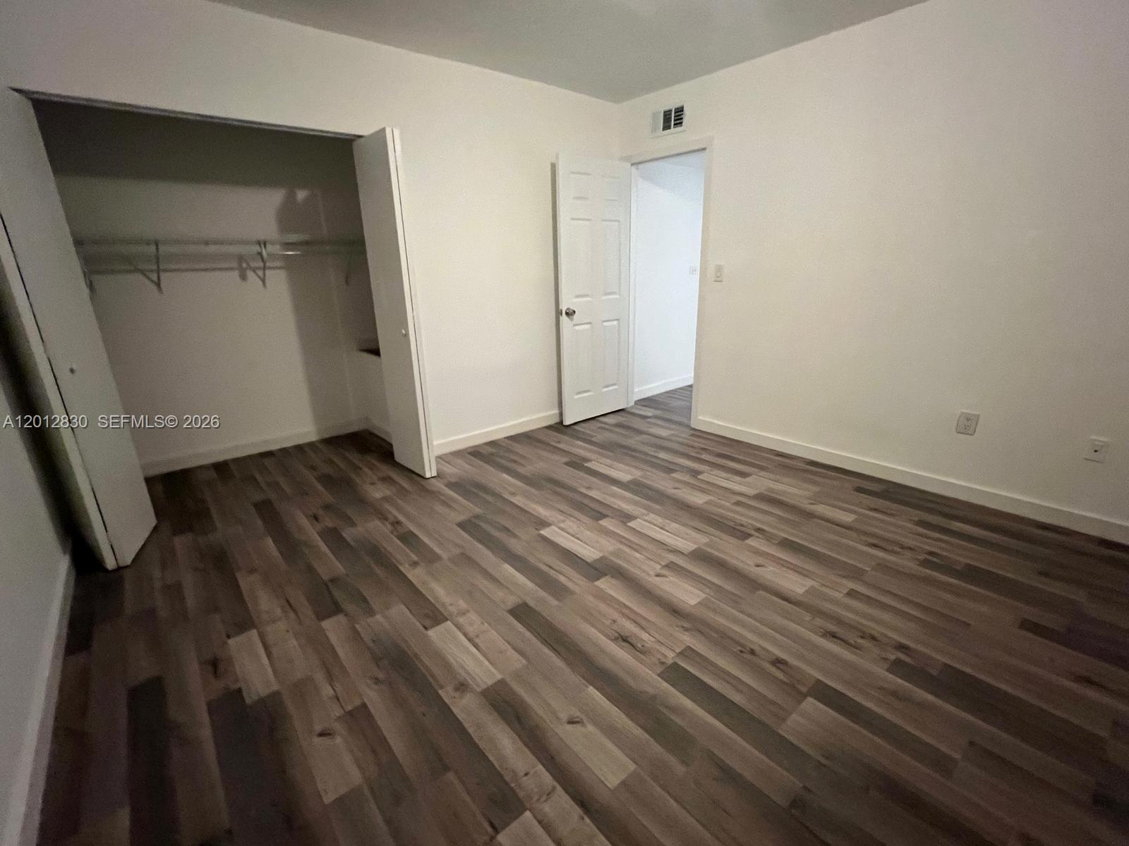 An empty bedroom features wood-look flooring, a white closet, and an open doorway — 1560 NE 151st St # 102, Miami FL 33162, MIAMI, FL