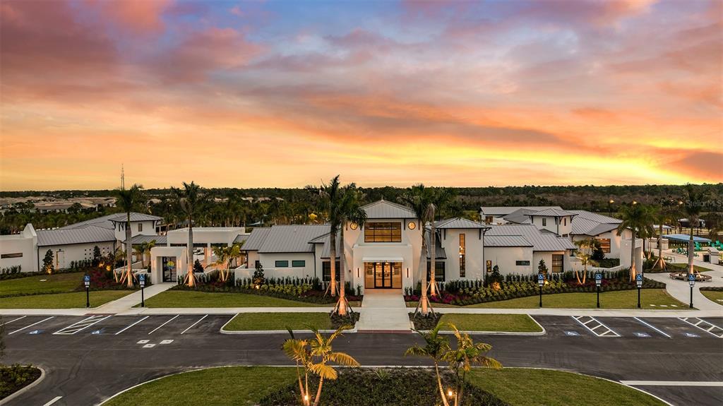An exterior view of a modern community clubhouse with palm trees at sunset — 18312 CHROMATA DRIVE, VENICE, FL