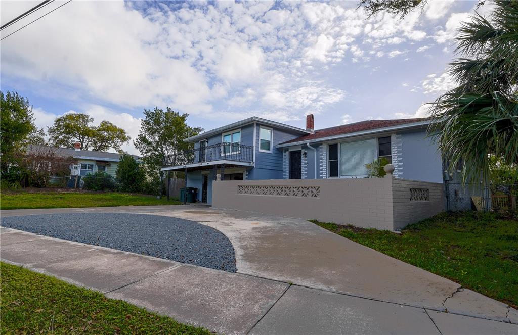 A two-story blue house features a front balcony, a low masonry wall, and a driveway — 1208 N HALIFAX AVENUE, DAYTONA BEACH, FL