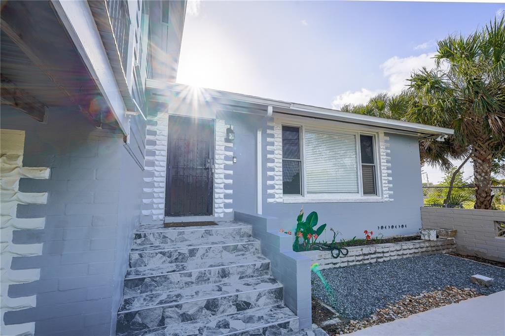 A light blue house exterior features a front door with stairs and a gravel garden — 1208 N HALIFAX AVENUE, DAYTONA BEACH, FL