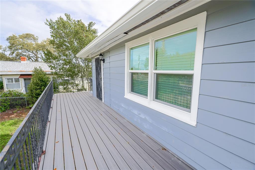 A gray elevated deck with a metal railing runs alongside a blue-sided house exterior — 1208 N HALIFAX AVENUE, DAYTONA BEACH, FL