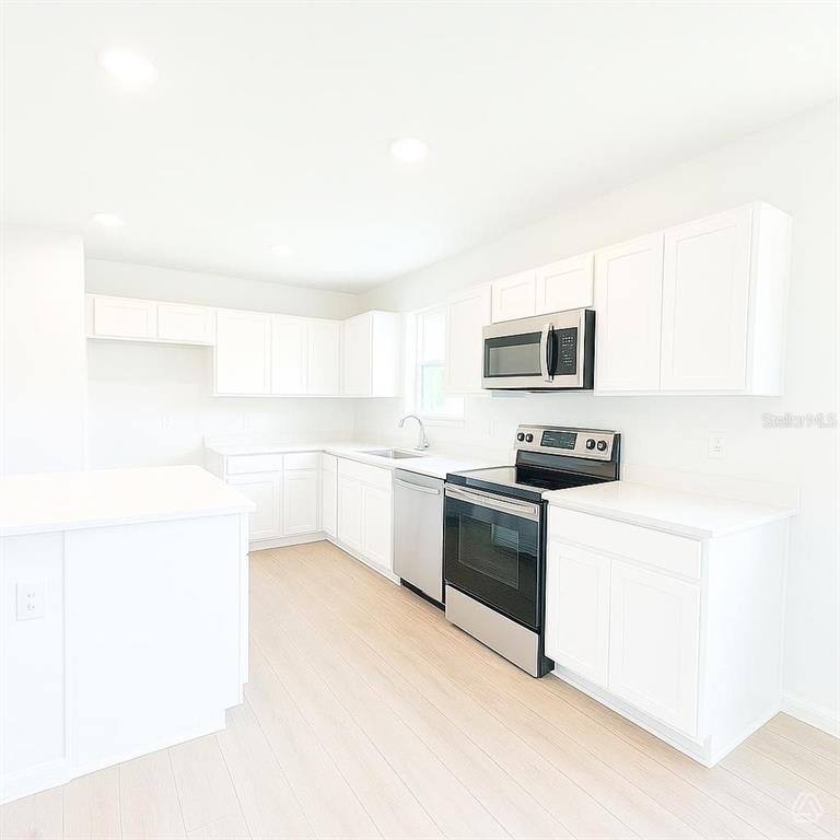 A modern kitchen features white cabinets, stainless steel appliances, and light-colored wood-look flooring — 13218 SASSAFRAS TRIAL, PARRISH, FL