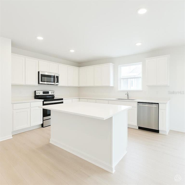A white kitchen features a central island, stainless steel appliances, and light wood-look flooring — 13218 SASSAFRAS TRIAL, PARRISH, FL
