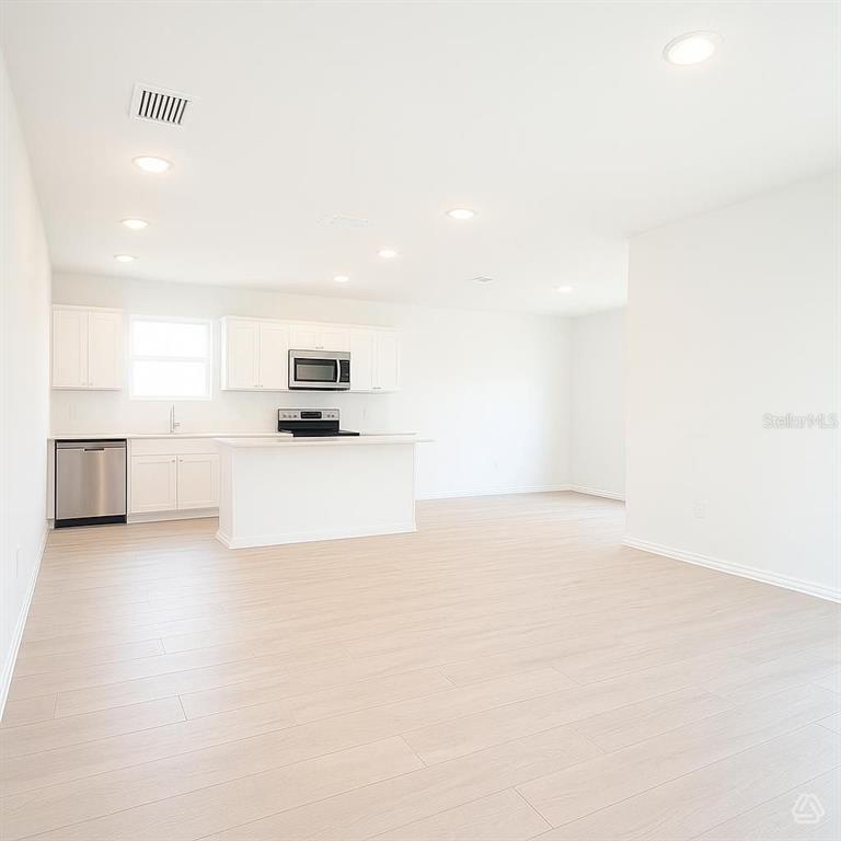 A bright, open-concept kitchen features white cabinetry, stainless steel appliances, and light wood-look flooring — 13218 SASSAFRAS TRIAL, PARRISH, FL