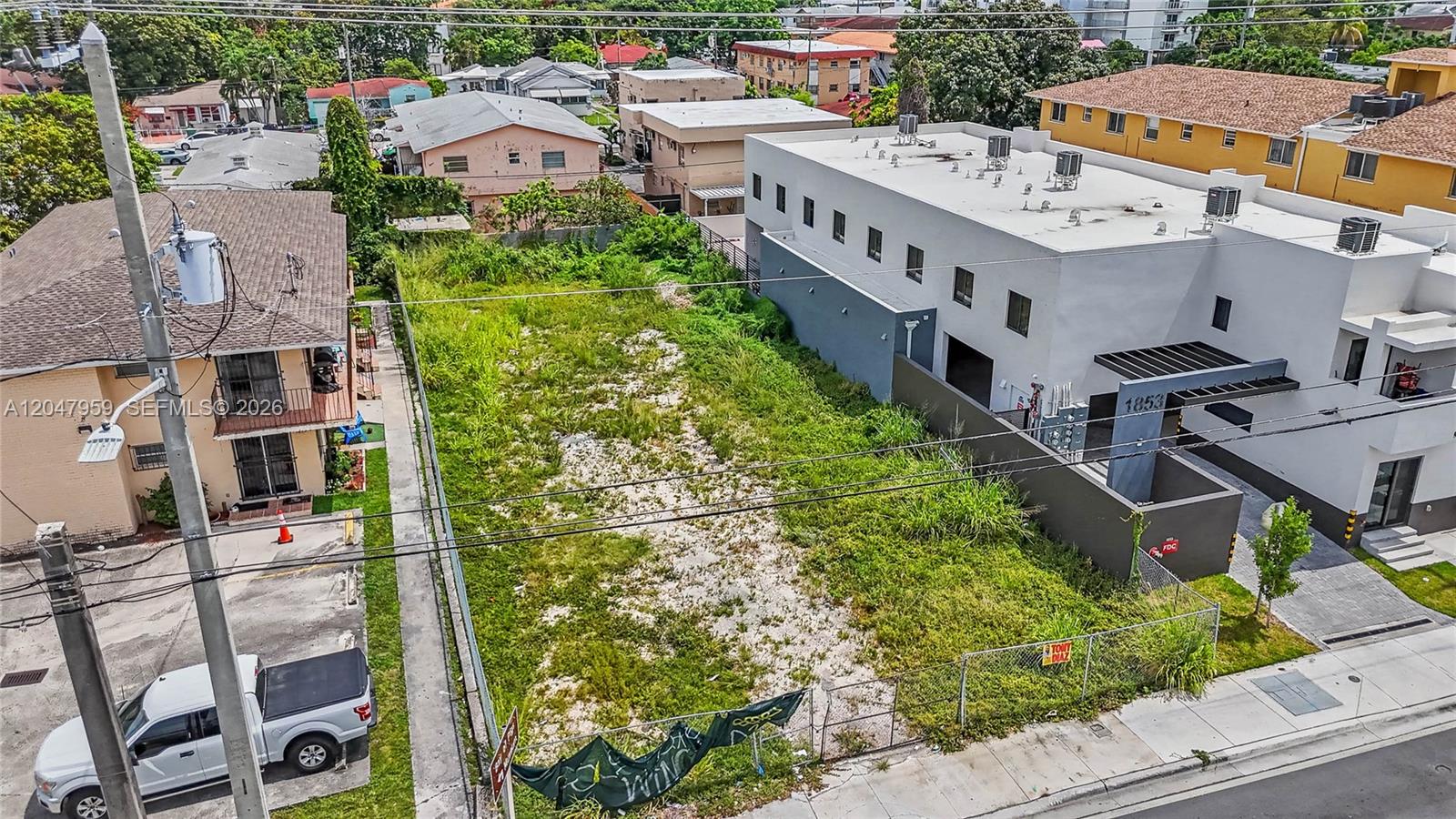 An aerial view shows a vacant, fenced-in rectangular lot situated between two residential buildings — 1877 SW 7th St, Miami FL 33135, MIAMI, FL