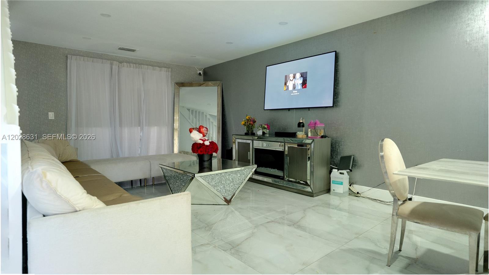 A living room features a mirrored coffee table, a wall-mounted television, and tiled flooring — 18499 NW 52nd Path, Miami Gardens FL 33055, MIAMI GARDENS, FL
