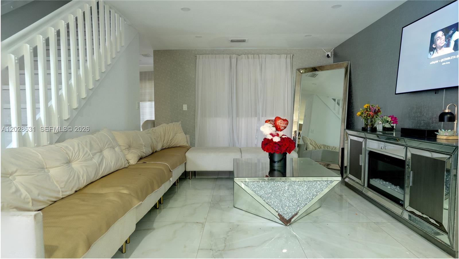A living room features a white sectional sofa, mirrored coffee table, and a wall-mounted television — 18499 NW 52nd Path, Miami Gardens FL 33055, MIAMI GARDENS, FL