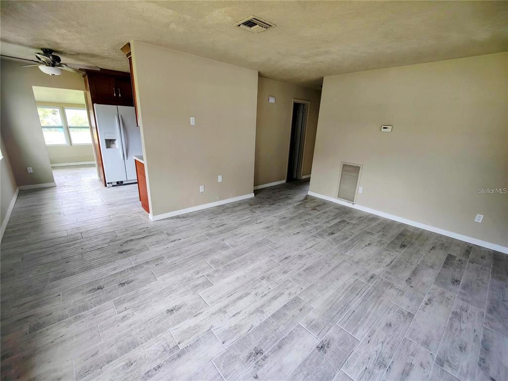 A living room with light wood-look tile flooring leads to a kitchen with a refrigerator — 190 DANFORTH DRIVE, PUNTA GORDA, FL