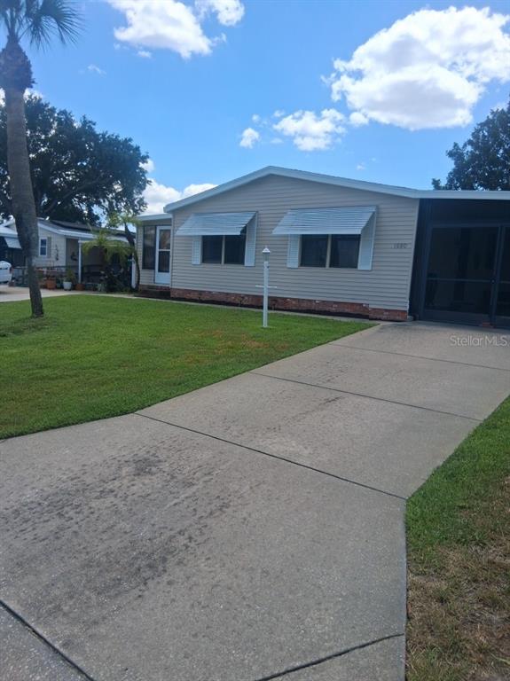 A single-story house with light siding, a concrete driveway, and a screened-in porch — 1550 HILLCREST DRIVE, THE VILLAGES, FL