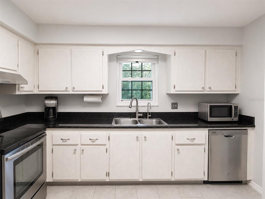 A kitchen features white cabinets, black countertops, stainless steel appliances, and a window above the sink — 1706 BELLEAIR FOREST DRIVE UNIT 244, BELLEAIR, FL