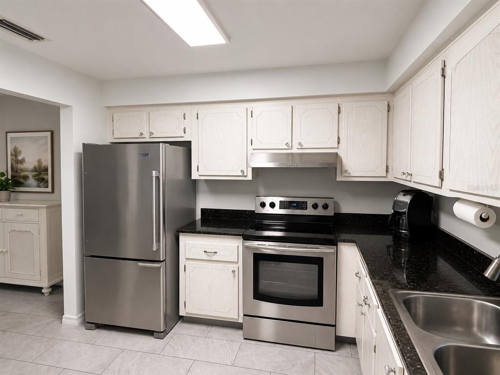 A kitchen features white cabinets, black granite countertops, and stainless steel appliances — 1706 BELLEAIR FOREST DRIVE UNIT 244, BELLEAIR, FL