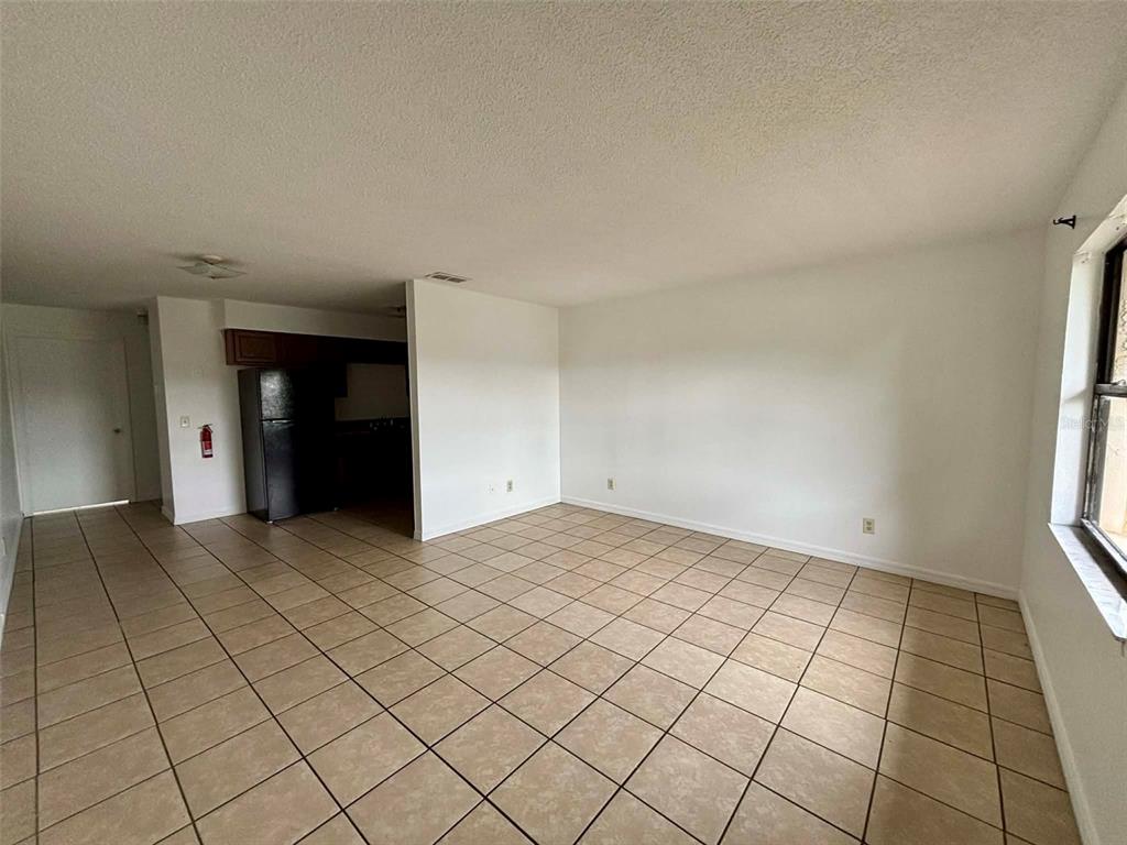 An empty living room with beige tile flooring and a view into a kitchen area — 503 N LANIER AVENUE, FORT MEADE, FL
