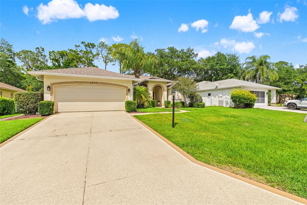 A single-story house with a beige exterior, a two-car garage, and a concrete driveway — 2593 CRYSTAL LAKE DRIVE, SPRING HILL, FL