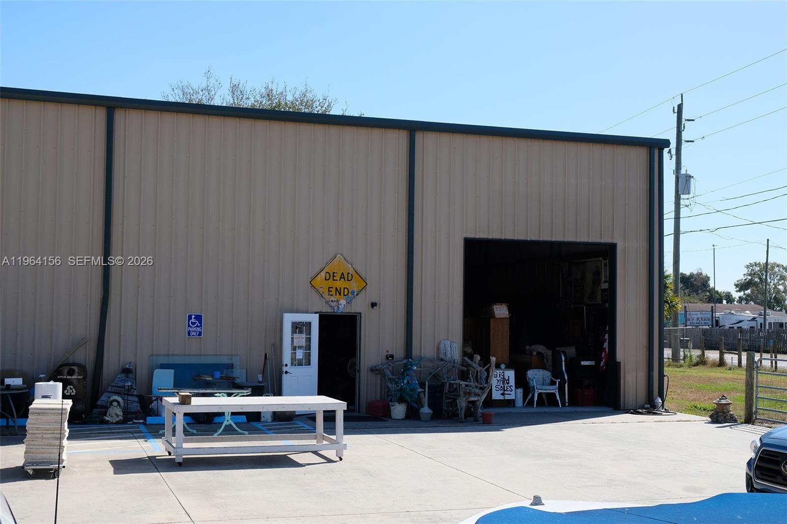 A tan metal warehouse building features a large open bay door and a pedestrian entrance — 5271 US HWY 441 SE, Okeechobee FL 34974, OKEECHOBEE, FL