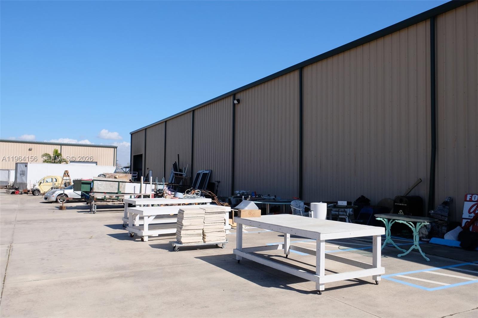 An exterior view shows a large metal warehouse building with work tables and equipment outside — 5271 US HWY 441 SE, Okeechobee FL 34974, OKEECHOBEE, FL