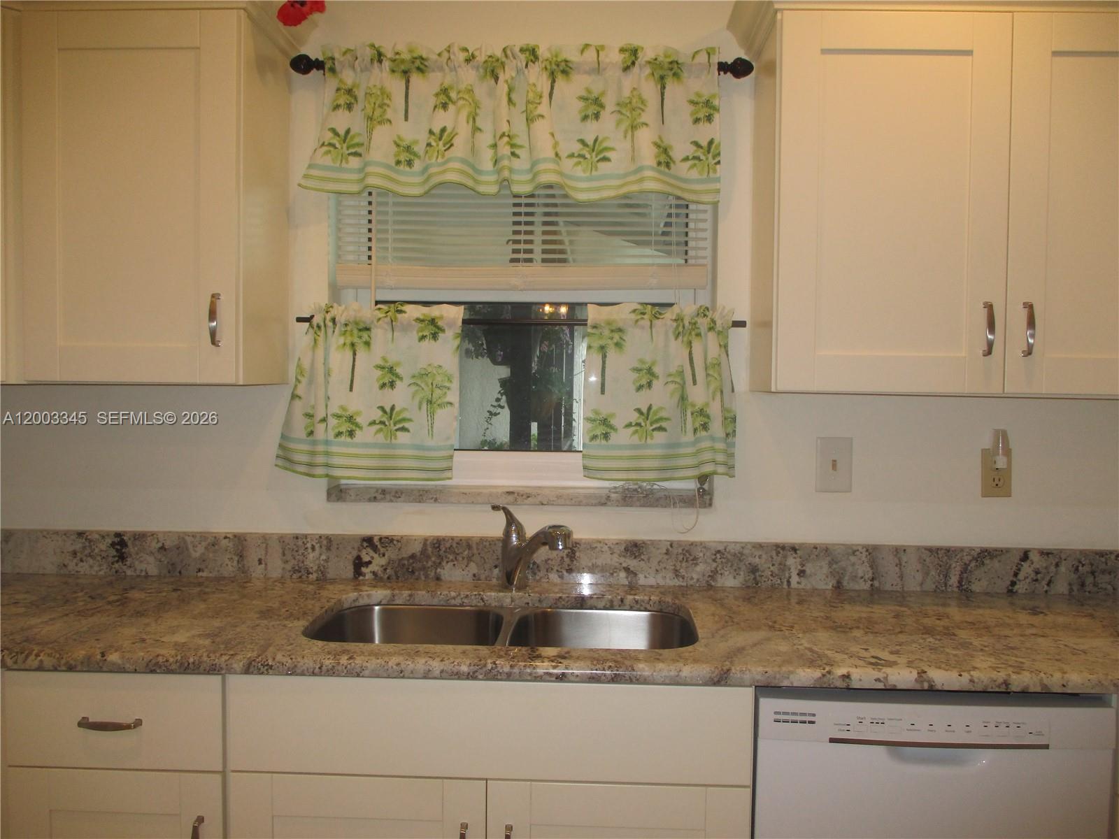 A kitchen sink area features white cabinets, granite countertops, and a window with palm-print curtains — 6531 SE Federal Hwy # S212, Stuart FL 34997, STUART, FL