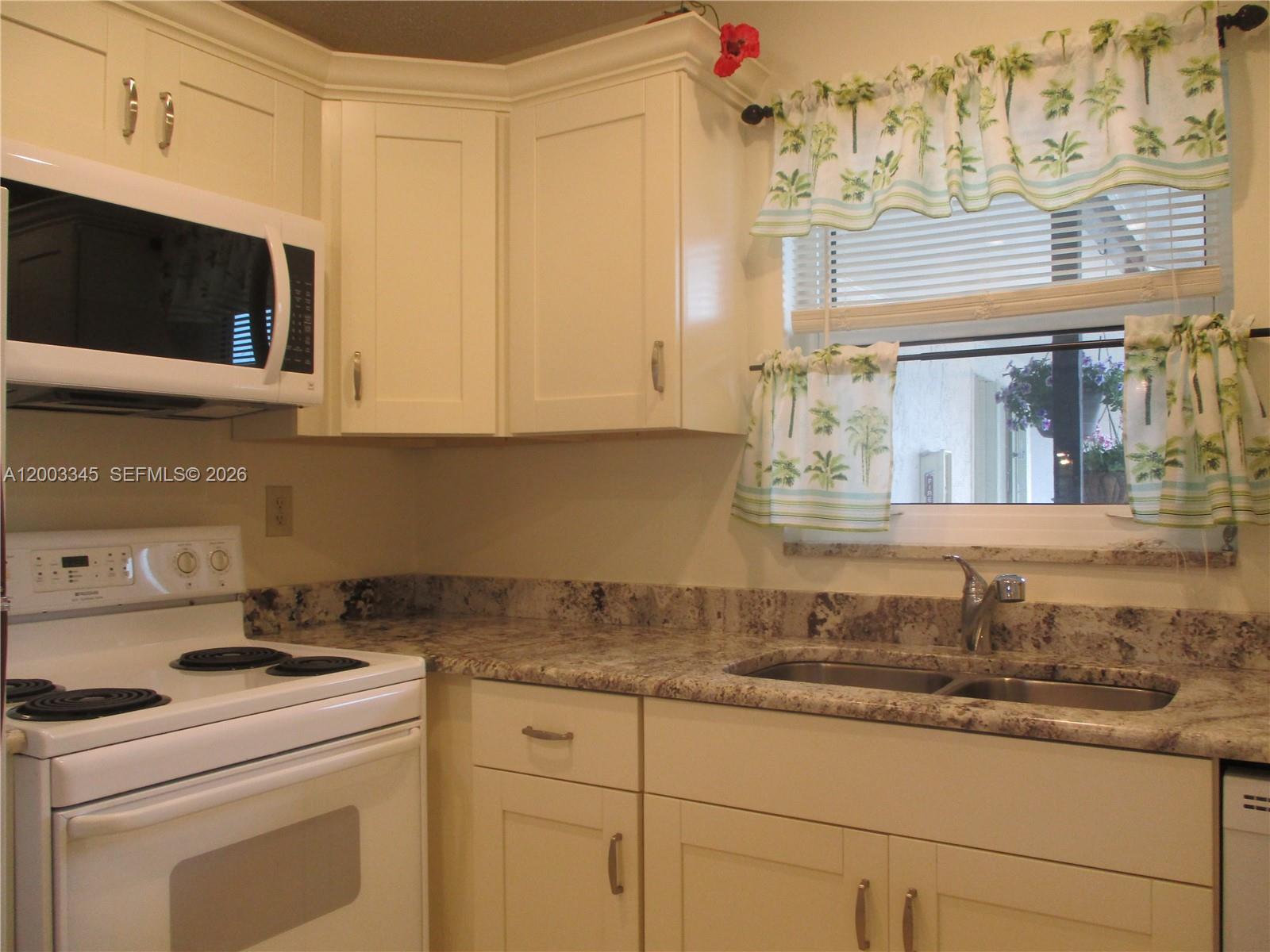 A kitchen features white cabinets, a white stove, a microwave, and granite countertops — 6531 SE Federal Hwy # S212, Stuart FL 34997, STUART, FL