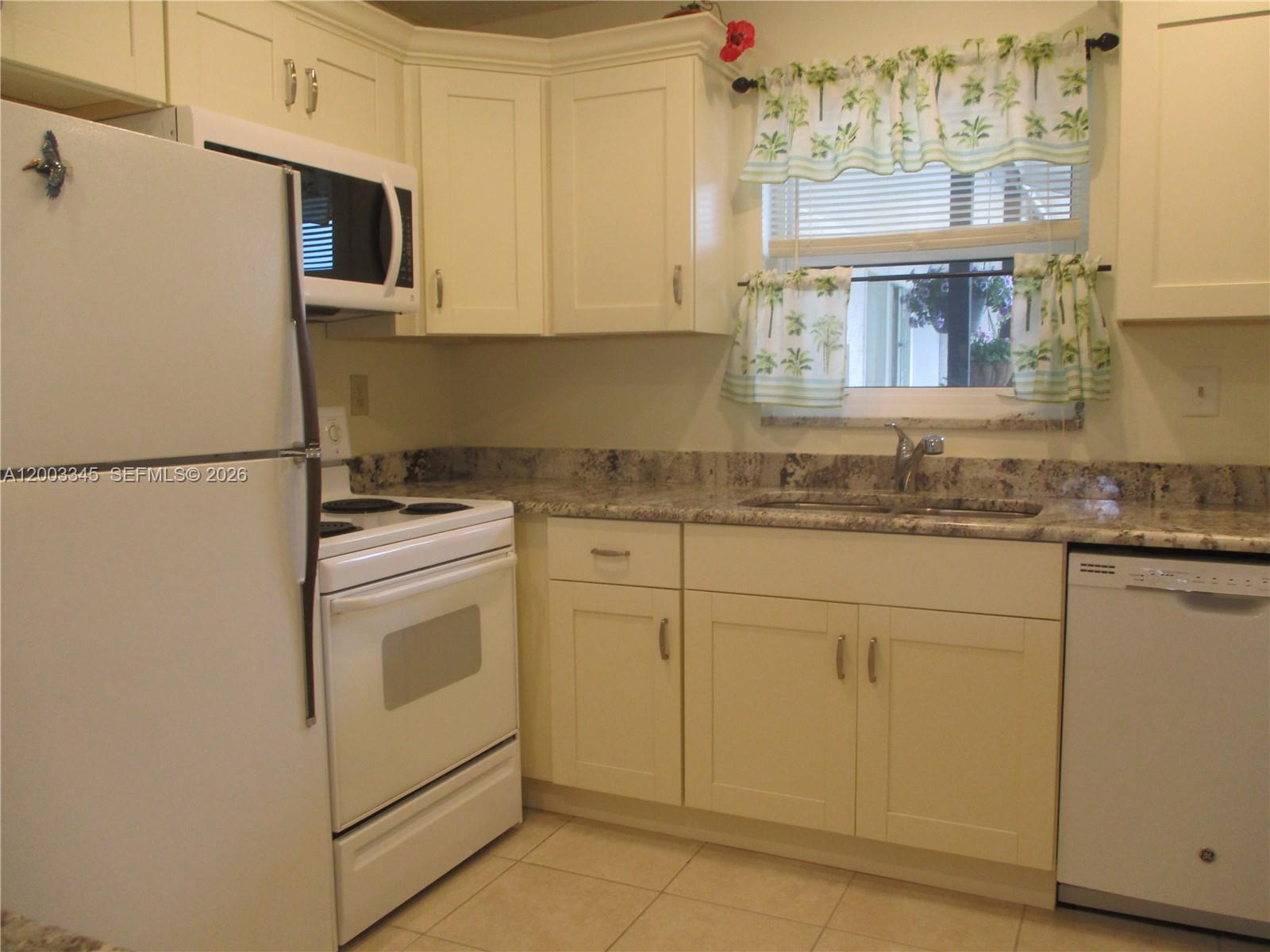 A kitchen features white cabinetry, granite countertops, a white stove, and a window with curtains — 6531 SE Federal Hwy # S212, Stuart FL 34997, STUART, FL