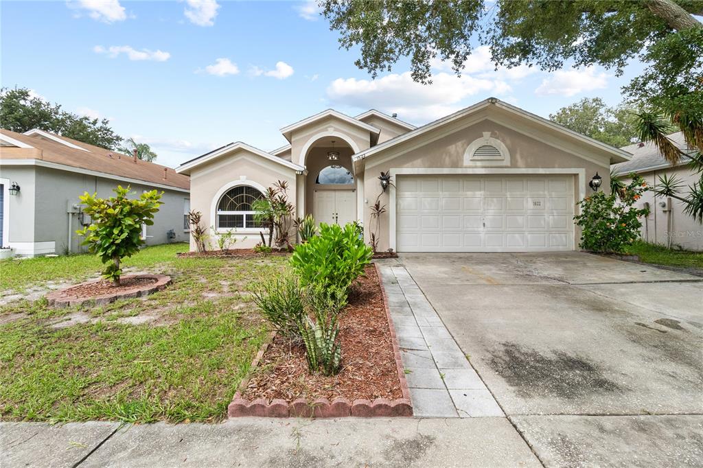 A single-story house with a beige stucco exterior, a two-car garage, and a landscaped yard — 1622 HULETT DRIVE, BRANDON, FL