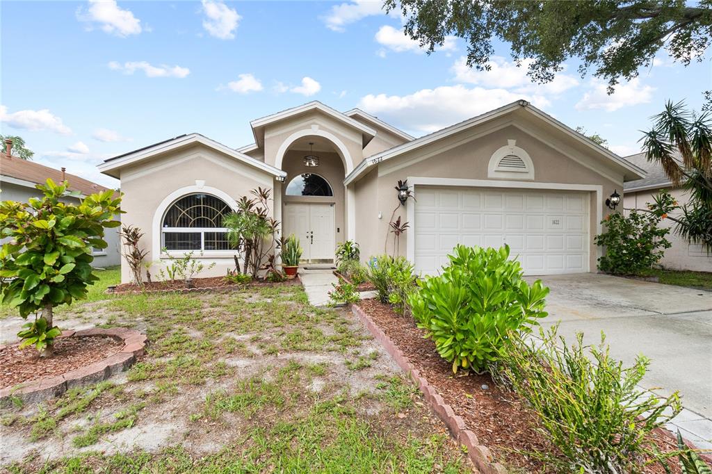 A single-story suburban house features a beige stucco exterior, a two-car garage, and arched windows — 1622 HULETT DRIVE, BRANDON, FL