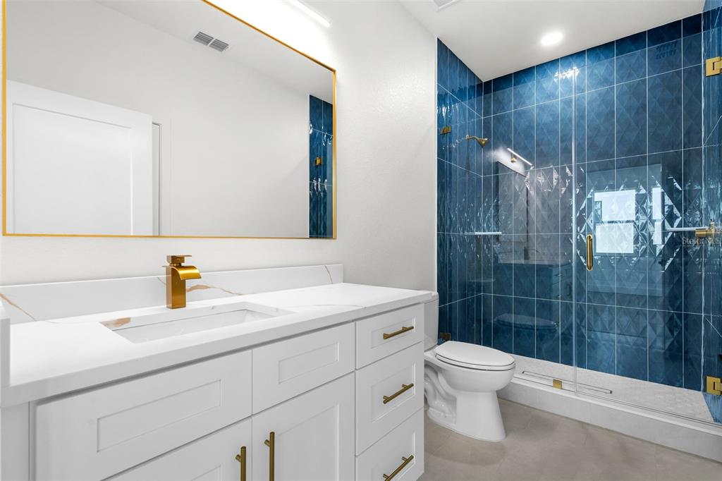 A bathroom features a white vanity with gold hardware, a mirror, and a blue-tiled shower — 2912 N 21ST STREET, TAMPA, FL